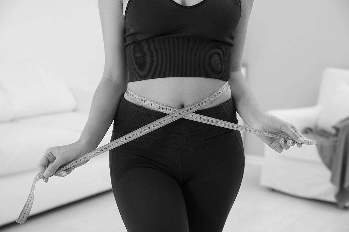 Slim woman measuring her waist at home, closeup. Weight loss